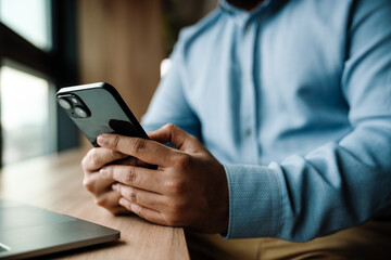 Close up of male hands using smartphone while sitting at table indoors