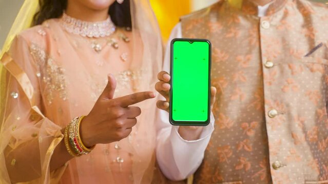 unrecognizable shot of muslim couple showing green screen mobile phone by looking at camera at home - concept of technology,promotion and recommending.