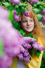 red-haired girl stands near a lilac bush 