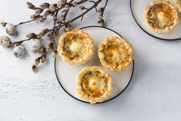 Mushroom julienne with quail egg and cheese in a puff pastry basket on a light blue background. Easter style with willow branches