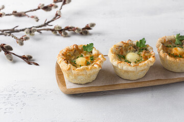 Mushroom julienne with quail egg and cheese in a puff pastry basket on a light blue background. Easter style with willow branches