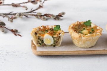 Mushroom julienne with quail egg and cheese in a puff pastry basket on a light blue background. Easter style with willow branches