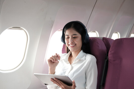 Cheerful Asian woman sitting on a plane and use the tablet while traveling