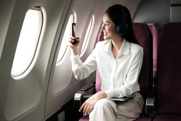 Joyful asian woman sits in the airplane and using tablet while go to travel