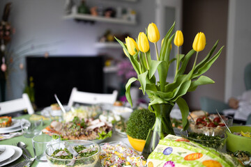 Home interior with easter decor. Spring flowers in a vases. Traditional Easter dishes with white borscht, sausage, eggs, salad and cakes on festive table in Poland