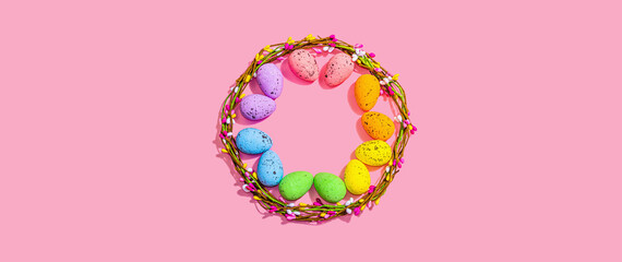 Obraz na płótnie Canvas Easter wreath with colorful eggs on pink background. Artificial floral decor, festive symbols