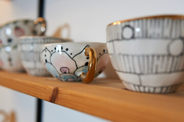Artistic handmade ceramic cups and mugs with golden details on a shelf