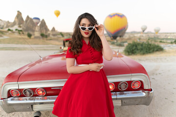 beautiful girl in retro style posing near a vintage red cabriolet car on background of balloons in Cappadocia.