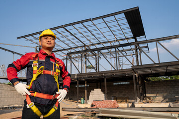 Construction worker wearing safety harness and excavator wearing orange reflective vest standing in front at construction site.