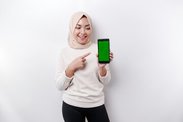 A happy Asian Muslim woman wearing a headscarf, showing her phone screen, isolated by white background