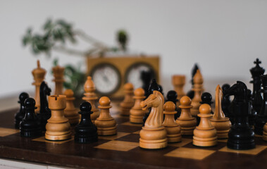 Wooden chess pieces and timer clock behind them out of focus