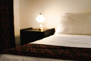 Night table with lamp besides bed out of focus