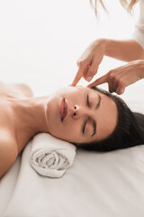 Obraz na płótnie Canvas Crop masseuse doing facial massage to female customer
