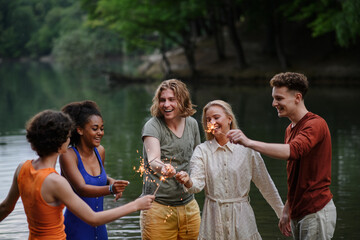 Happy group of friends lighting sparklers and enjoying freedom at beach during sunset