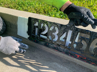 City worker painting address on street curbs using stencil numbers with white and blank paint
