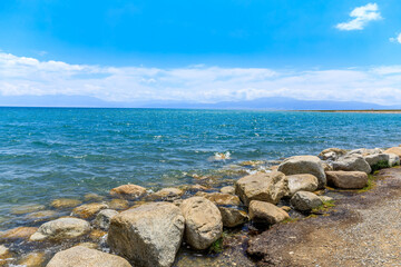 Fototapeta na wymiar Blue Sayram Lake natural scenery in Xinjiang, China. Clear lake water and rocks under blue sky.