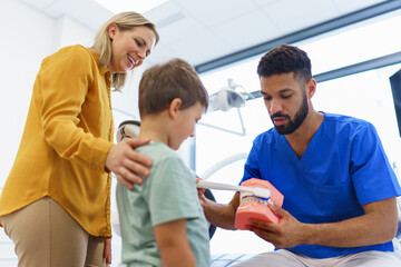 Young multiracial dentist showing little boy how to clean teeth, concept of children oral hygiene,prevention and dental health.