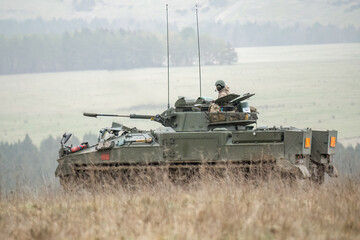 British army Warrior FV510 with commander in action, moving across countryside