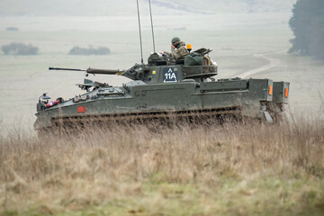 British army Warrior FV510 with commander in action, moving across countryside