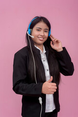 A typical female BPO employee in her early 20s and wearing a wired headset making a thumbs up sign. An outstanding member of the workforce. Isolated on a pink background.