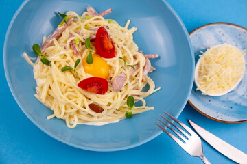 Pasta with cheese and egg, bacon and tomatoes, microgreens. Food in a blue plate. Homemade carbonara pasta. Lunch on the table top view. Italian spaghetti with ham, cream