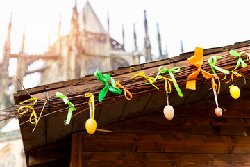 Multicolored bright easter eggs decoration hanged on paper ribbons on wooden house roof against old cathedral church in historical center european city market square. Holiday decoration St Vitus Dome