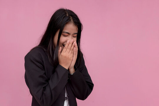 An asian lady employee breaks into laughter after hearing a funny joke. Isolated on a light pink background.