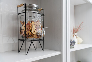 A decorative glass jar stands in a white kitchen cabinet.