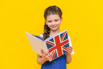 English for children. A little girl holds a textbook with an English flag in her hands. Children's...