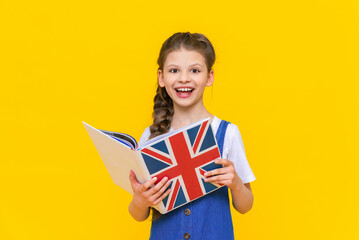 The child is learning British English. Portrait of a little girl holding a book. Education of children. Learning foreign languages. yellow isolated background.