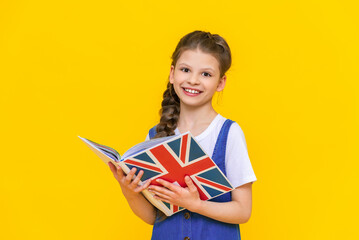 The child is learning British English. Portrait of a little girl holding a book. Education of...