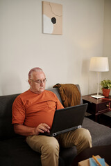 Senior man sitting on couch and working on laptop