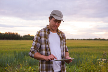 Farmer with a tablet computer in front of a sunset agricultural landscape. Countryside field. The...