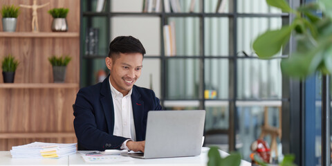 Smiling Asian Banker makes financial report and studies annual figures, analyzes profits. Accountant checks status of financial