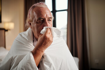 Portrait of senior man wrapping in duvet and blowing nose