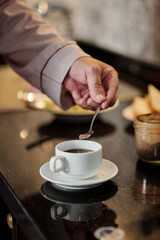 Fototapeta na wymiar Hand of senior man putting spoon of brown sugar in cup of coffee