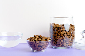 Dry pet food in a glass jar, bowl and water close-up on a white background.
