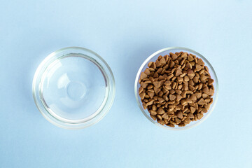 Dry pet food in a glass jar and bowl close-up on a blue background. View from above