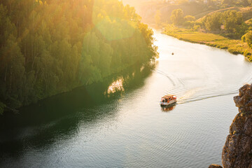 the landscape of a summer evening is a view from the mountain to the river on which a boat carrying people sails