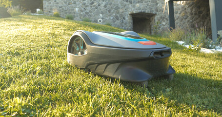 CLOSE UP: Side view of robotic lawn mower trimming green grass in modern garden