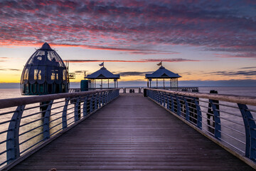 Seebrücke mit Tauchgondel in Grömitz beim Sonnenaufgang. Wolken werden rot angeleuchtet