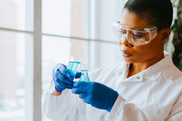 african american woman student intern with conducts an experiment with beaker and liquid in protective glasses, studies viruses and bacteria, scientist doctor of biology working on scientific project