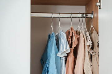 Children's clothes, girls' dresses hang on hangers in an open closet, dressing room