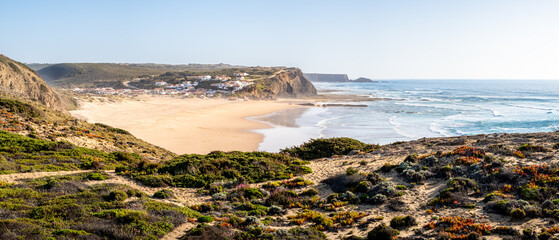 Panoramic view of Praia de Monte Clérigo beach at low tide with a small village and the vast...