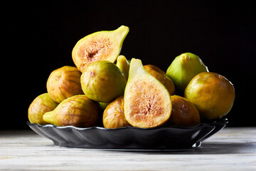 Many fresh figs on dish. Whole ripe, fresh, sweet figs and one fig sliced on dark background....