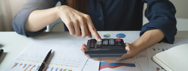 Women business people use calculators to calculate the company budget and income reports on the desk in the office.