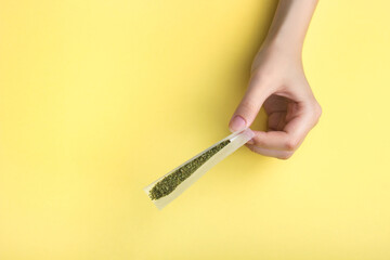 In female hands, paper for a joint, a filter and crushed medical marijuana.  Against a bright banana yellow background