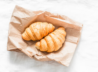 Fresh crispy croissants on a paper bag on a light background