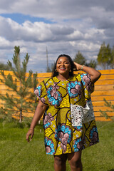 Summer portrait of beautiful african american woman in colourful dress wear standing on backyard. Suburban lifestyle and chilling on weekend in countryside and inclusion with diversity concept