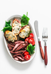 Delicious appetizer, tapas, lunch plate - beef steak, vegetables salad and roasted potatoes with blue cheese on a light background, top view